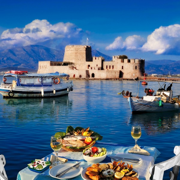 A table prepared for lunch & fishing boats in the bay in front of Bourtzi castle in Nafplio, Greece